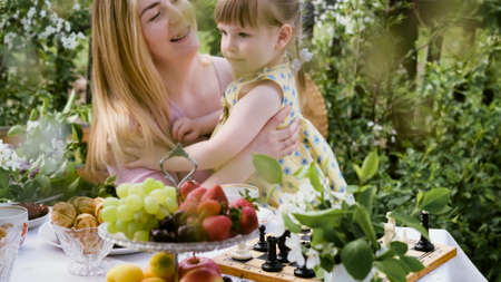 A young woman and little daughter are sitting in the backyard at a table with ripe organic berries...