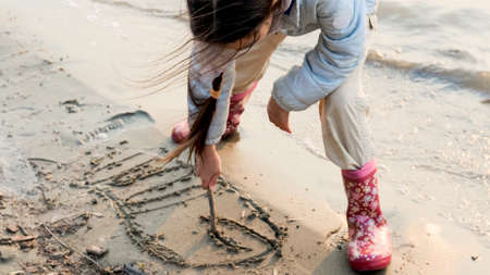 Little girl draws a big whale on the sand of the beachの写真素材
