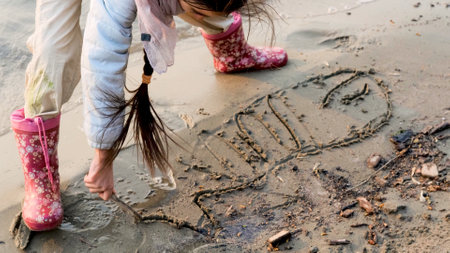 Little girl draws a big whale on the sand of the beachの写真素材