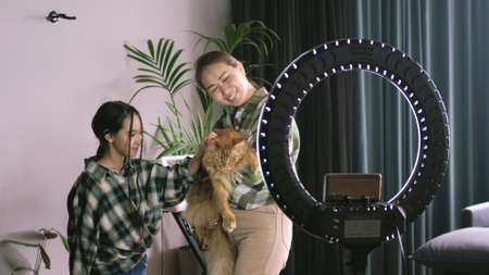 A little girl and mother pose for a video blog with a domestic ginger Maine Coon cat. Family vlog about petsの写真素材