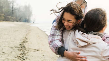 Happy family is resting and having fun together in nature on the river bank in spring. Teenage daughter hugging mom and laughing.の写真素材