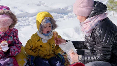 An Asian mother treats children with cookies and hot tea from a thermos. Winter picnic in natureの写真素材