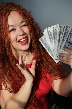 A rich red-haired woman holds a wad of dollars in her hand. Concept of financial successの写真素材