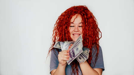 A rich red-haired woman holds a wad of dollars in her hand. Concept of financial successの写真素材