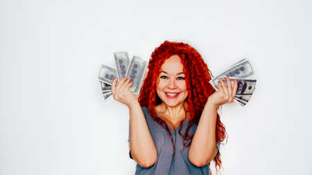 A rich red-haired woman holds a wad of dollars in her hand. Concept of financial successの写真素材