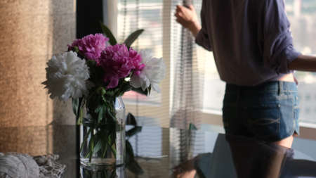 A young woman goes to the window and opens the curtains, enjoying the sunny morning.