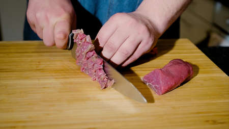 Close-up of a chef skillfully slicing raw meat on a cutting board.の写真素材