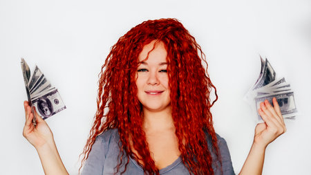 A rich red-haired woman holds a wad of dollars in her hand. Concept of financial successの写真素材