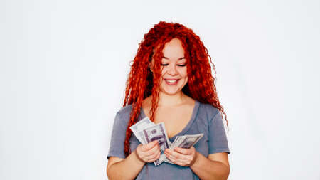 A rich red-haired woman holds a wad of dollars in her hand. Concept of financial successの写真素材