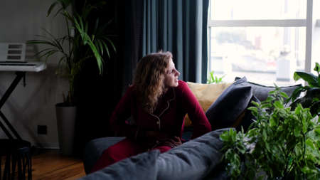 Stressed young woman lying on sofa, embracing belly, suffering from stomachache. Unhappy 20s girl having menstrual painful feelings, resting on sofa. Gastritis, abdominal or period pain concept.の写真素材