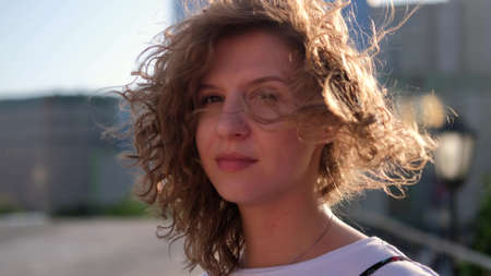 Portrait of a cute curly haired woman smiling charmingly while standing in the middle of a modern cityscape. Happy young woman enjoying life.の写真素材