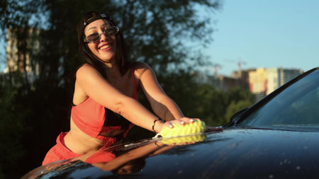 A young woman washes a car outside outdoors in the light of the setting sun.の写真素材