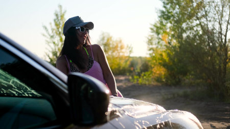 A young woman washes a car outside outdoors in the light of the setting sun.の写真素材