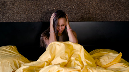 Young annoyed woman suffers from insomnia due to bad noisy neighbors. Angry beautiful woman disturbed by loud noise trying to sleep.の写真素材