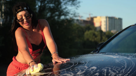 A young woman washes a car outside outdoors in the light of the setting sun.の写真素材