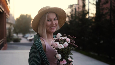 Portrait of a cute hipster girl smelling a bouquet of flowers outdoors. Close-up of a cute woman holding a flower bouquet in her hands outside. Smiling woman with flowers on a city street.の写真素材