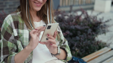 Woman typing a message outside an office building. A girl uses a smartphone while sitting on a street bench.の写真素材