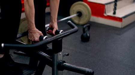 A middle-aged woman trains her arm muscles using a simulator in the gym.の写真素材