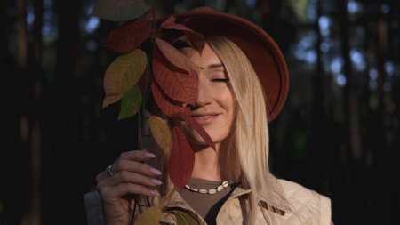 Portrait of a beautiful woman in a brown hat with autumn leaves to her hand. A woman is embroidered...