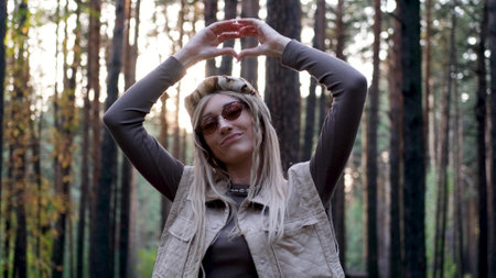 Hippie woman with a smile on her face holds her hands in the shape of a heart while standing in the...