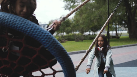 Two happy sisters are swinging. A cute little girl is pushing the swing, swinging it.の写真素材