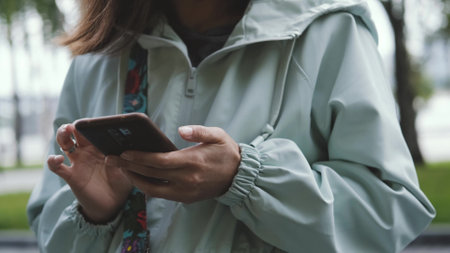 Close-up of a womans hands holding a smartphone and typing a message on the street.