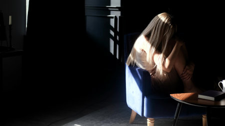 A depressed young beautiful woman sits alone in an armchair in the dark, hugs her knees and is sad. Loneliness sad woman thinks about grief, problems of life. Negative emotions andの写真素材