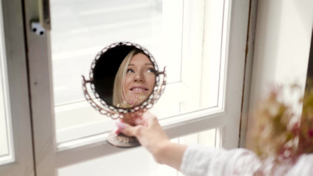 Beautiful blonde and admires herself in front of a mirror in a bright room near the windowの写真素材