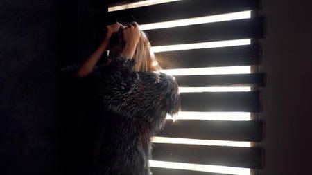 A depressed blonde stands in the dark, near a barred window. Loneliness sad woman thinks about...