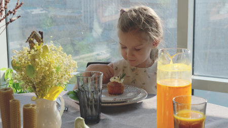 A little girl in a smart dress sits at a festive Easter table and eats a delicious cupcake