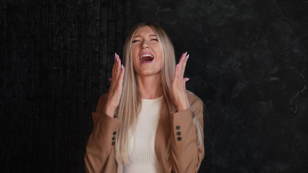 Portrait of an angry, angry and unhappy woman screaming loudly with palms up against a dark background. The woman symbolizes irritation, mental disorder.の写真素材