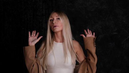 Portrait of a blonde woman in a business suit against a dark wall. The blonde is unhappy with the circumstances, makes a negative sign with her handsの写真素材