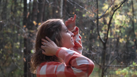 A beautiful curly-haired woman raises her hands to her eyes with a smile, looks at the sky, walks...