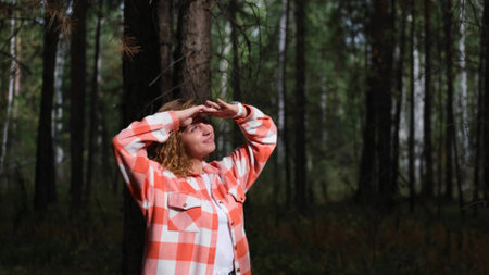 A beautiful curly-haired woman raises her hands to her eyes with a smile, looks at the sky, walks...