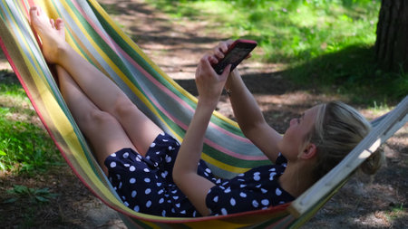 Young woman is resting outdoors in summer. The blonde lies in a hammock and looks into her...