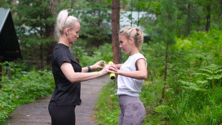 Fitness. Personal trainer taking notes while woman exercising outdoors. Two pretty sportswomen are engaged in fitness in the forest.の写真素材