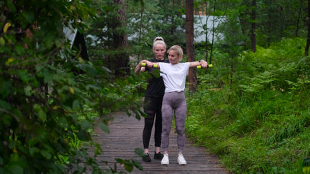 Fitness. Personal trainer taking notes while woman exercising outdoors. Two pretty sportswomen are...