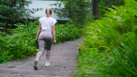 Beautiful sportswoman doing squats, lunges with dumbbells in the forest, during summer outdoor...