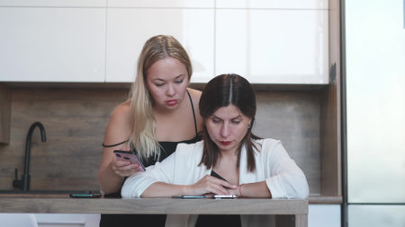 One on one meeting. Two young business women are sitting at a table at home. The girl shows her...