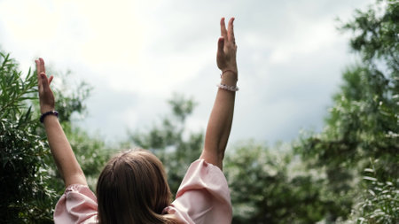 A young woman raises her hands up, the woman is wearing a pink long dress in boho style. A woman is enjoying the beautiful weather. She thanks God for her life and a beautiful day.の写真素材