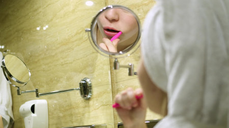 Beautiful woman looks at her reflection in the mirror, brushes her teeth, looking in the mirror. Home bathroom and lifestyle.の写真素材