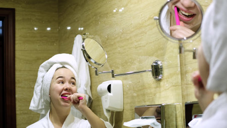 Beautiful woman looks at her reflection in the mirror, brushes her teeth, looking in the mirror. Home bathroom and lifestyle.の写真素材