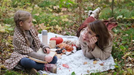 Young mother with her little daughter in an autumn park having picnicの写真素材