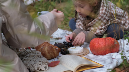Young mother with her little daughter in an autumn park having picnicの写真素材