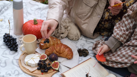 Young mother with her little daughter in an autumn park having picnicの写真素材