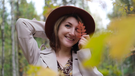 Cute woman in brown hat holding fallen leaves in autumn park. Autumn season.