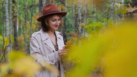 Cute woman in brown hat holding fallen leaves in autumn park. Autumn season.