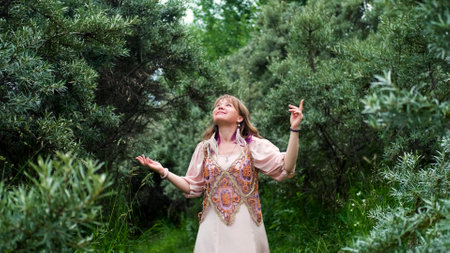 A young woman raises her hands up, the woman is wearing a pink long dress in boho style. A woman is enjoying the beautiful weather. She thanks God for her life and a beautiful day.の写真素材