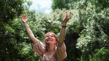 A young woman raises her hands up, the woman is wearing a pink long dress in boho style. A woman is enjoying the beautiful weather. She thanks God for her life and a beautiful day.の写真素材