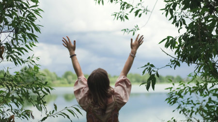 A young woman raises her hands up, the woman is wearing a pink long dress in boho style. A woman is enjoying the beautiful weather. She thanks God for her life and a beautiful day.の写真素材